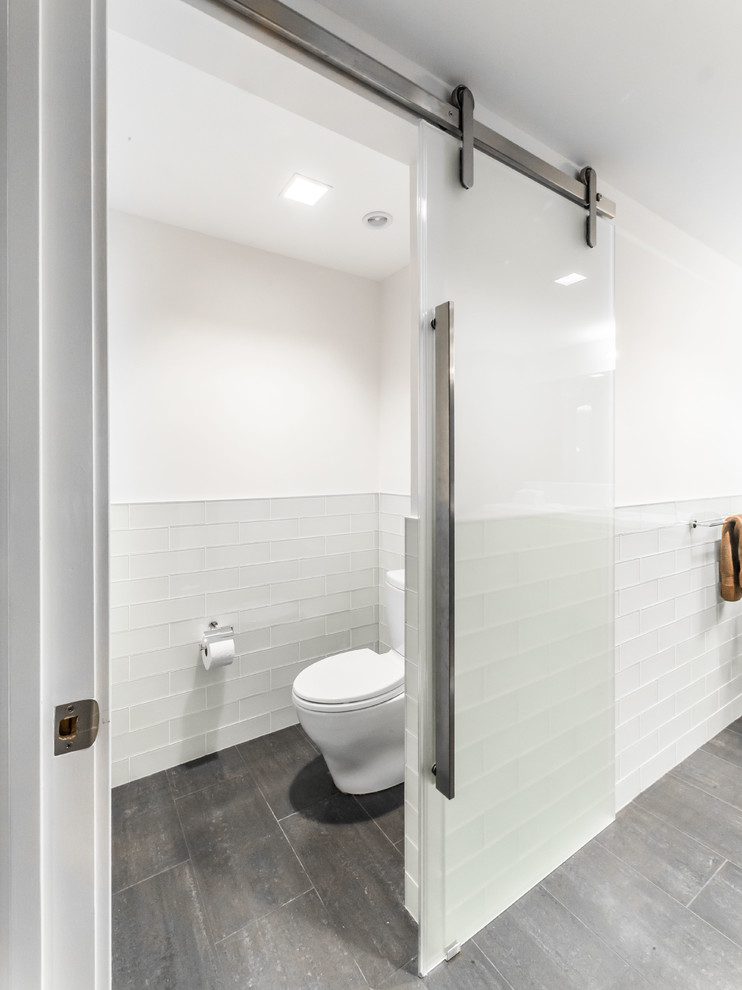 This is an example of a mid-sized modern 3/4 bathroom in New York with flat-panel cabinets, distressed cabinets, a corner shower, a two-piece toilet, white tile, glass tile, white walls, porcelain floors, an undermount sink and marble benchtops.