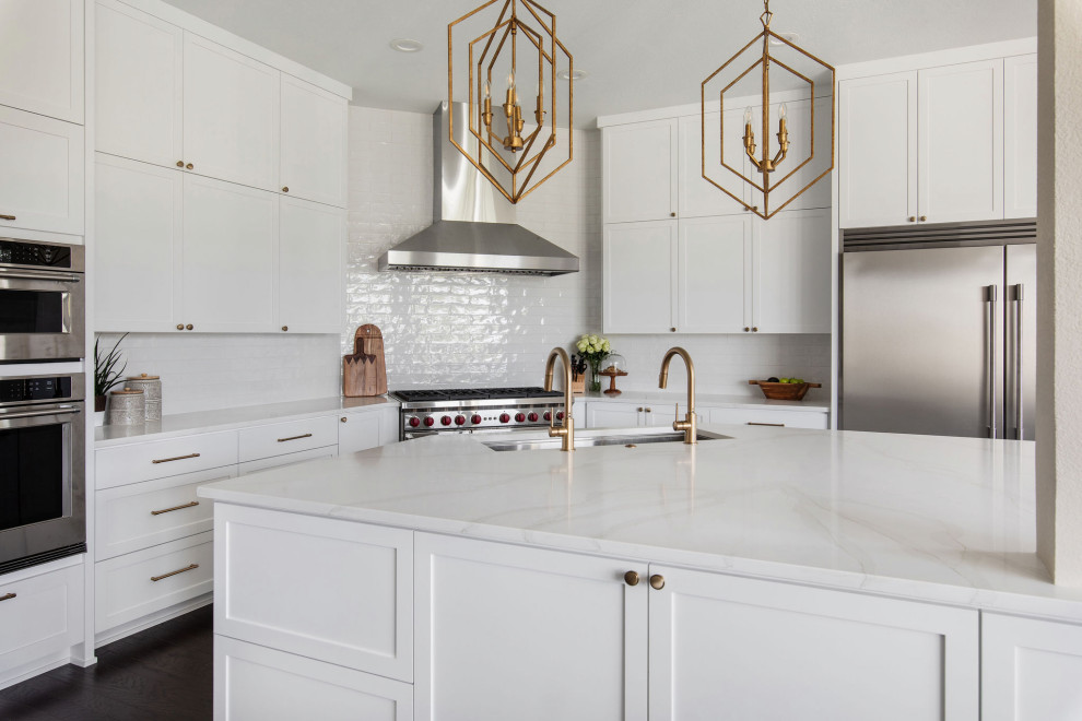 Open concept kitchen - large transitional l-shaped dark wood floor and brown floor open concept kitchen idea in Austin with an undermount sink, shaker cabinets, white cabinets, quartz countertops, white backsplash, ceramic backsplash, stainless steel appliances, an island and white countertops