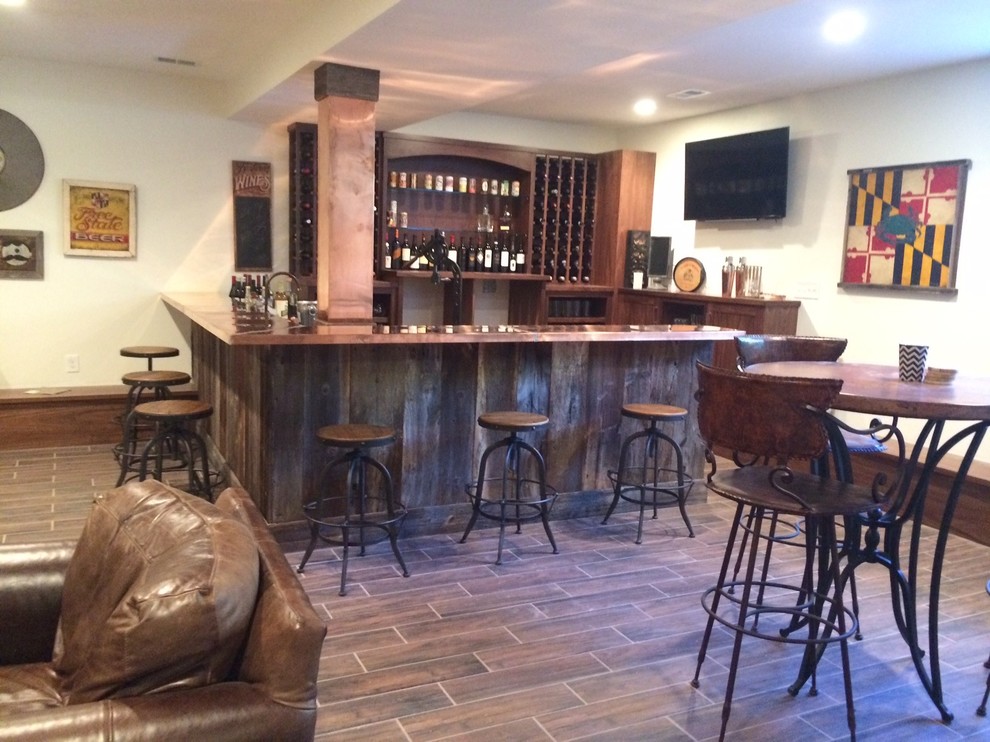 Large industrial u-shaped seated home bar in DC Metro with an undermount sink, recessed-panel cabinets, medium wood cabinets, copper benchtops and porcelain floors.