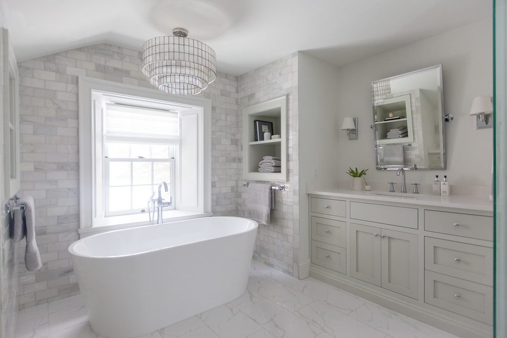 This is an example of a mid-sized contemporary master bathroom in Toronto with shaker cabinets, grey cabinets, a freestanding tub, an alcove shower, a one-piece toilet, white tile, marble, white walls, marble floors, an undermount sink, engineered quartz benchtops, white floor and a hinged shower door.