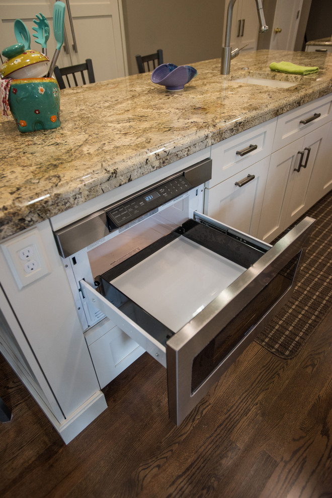 Large transitional u-shaped medium tone wood floor and brown floor eat-in kitchen photo with an undermount sink, shaker cabinets, white cabinets, granite countertops, beige backsplash, travertine backsplash, paneled appliances and an island