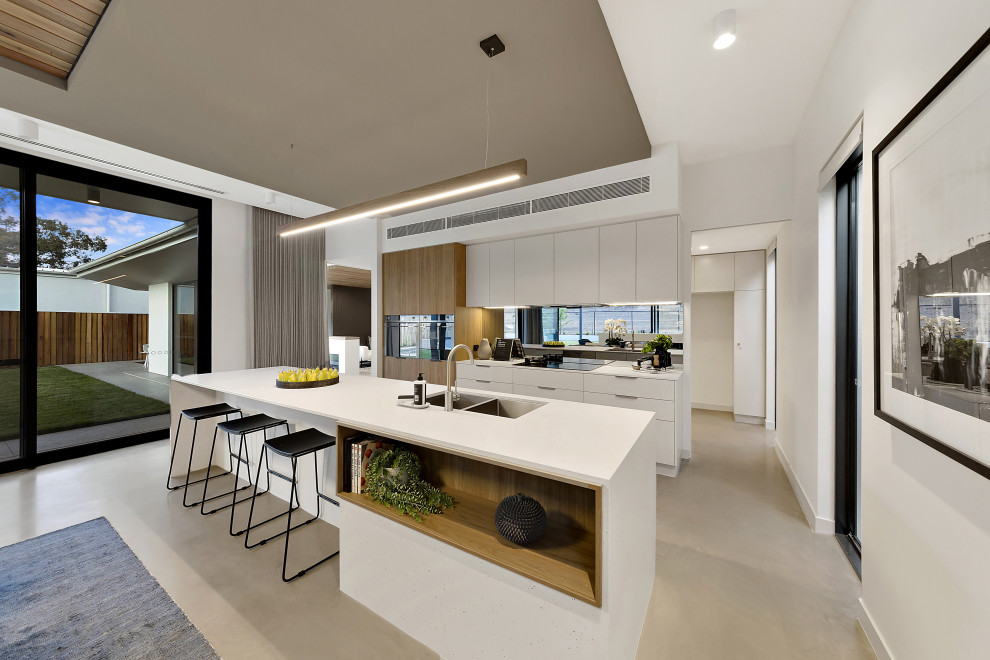 Mid-sized contemporary single-wall eat-in kitchen in Canberra - Queanbeyan with an undermount sink, flat-panel cabinets, white cabinets, quartz benchtops, white splashback, subway tile splashback, concrete floors, with island, grey floor and white benchtop.