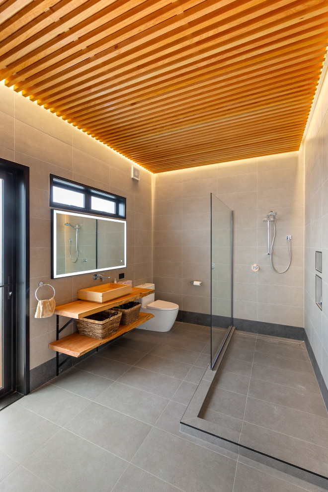 Photo of an asian bathroom in Auckland with open cabinets, light wood cabinets, an open shower, gray tile, grey walls, a vessel sink, wood benchtops, grey floor, an open shower, a niche, a single vanity, a built-in vanity, wood and wood walls.
