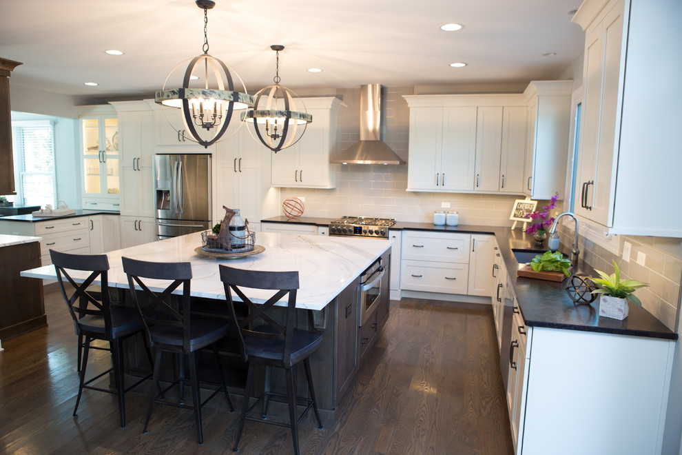 Example of a large transitional l-shaped medium tone wood floor eat-in kitchen design in Chicago with an undermount sink, recessed-panel cabinets, white cabinets, quartz countertops, gray backsplash, ceramic backsplash, stainless steel appliances and an island