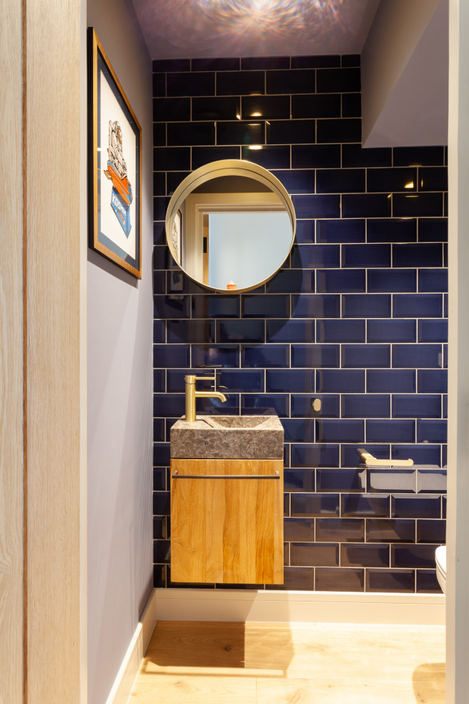 Cette photo montre un WC suspendu moderne en bois clair avec un carrelage bleu, des carreaux de céramique, un lavabo intégré, un plan de toilette en granite et meuble-lavabo suspendu.