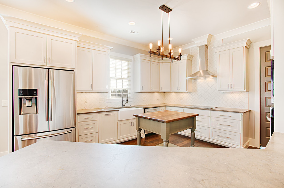 Kitchen - mid-sized transitional kitchen idea with a farmhouse sink, white cabinets, limestone countertops, white backsplash, ceramic backsplash, stainless steel appliances and an island
