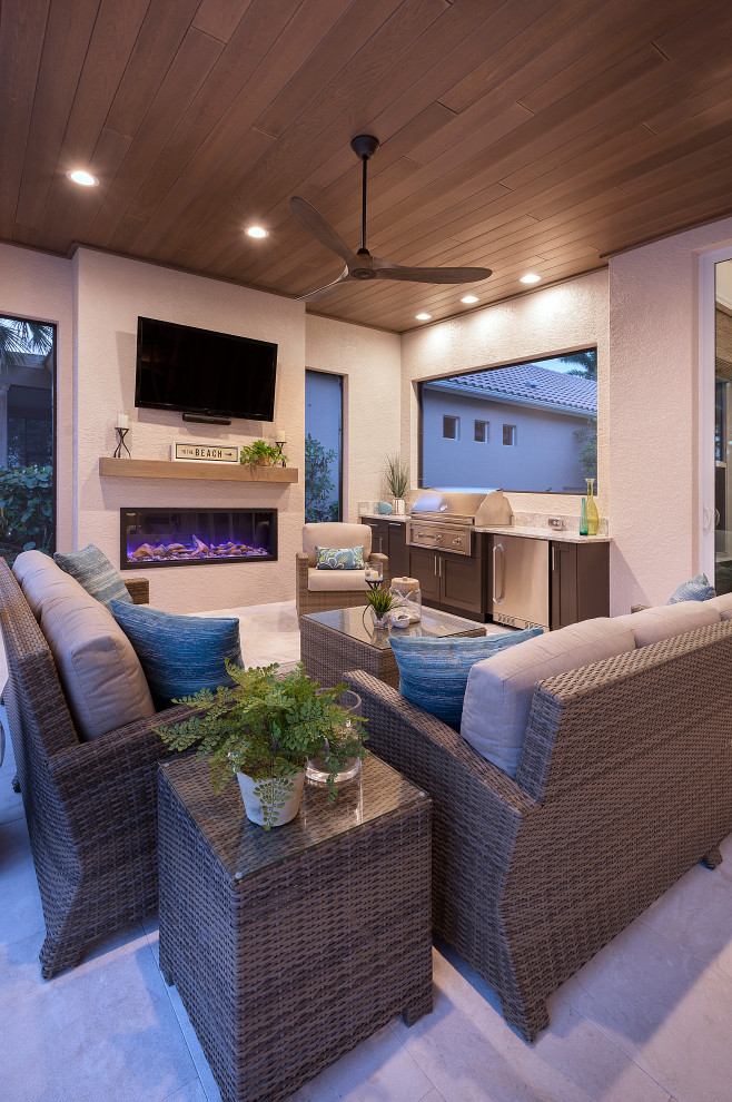 Réalisation d'une grande terrasse arrière design avec une cuisine d'été, des pavés en pierre naturelle et une extension de toiture.