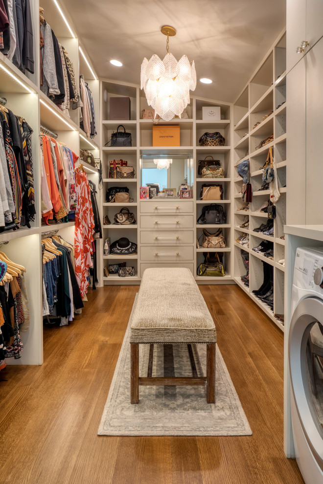 This is an example of an expansive beach style gender-neutral walk-in wardrobe in Other with flat-panel cabinets, white cabinets, medium hardwood floors and brown floor.