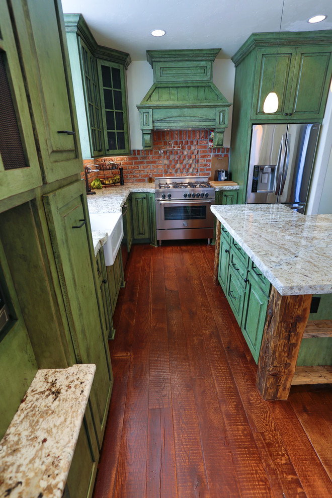 Design ideas for a mid-sized eclectic l-shaped eat-in kitchen in Portland with a farmhouse sink, raised-panel cabinets, green cabinets, granite benchtops, red splashback, stainless steel appliances, medium hardwood floors and with island.