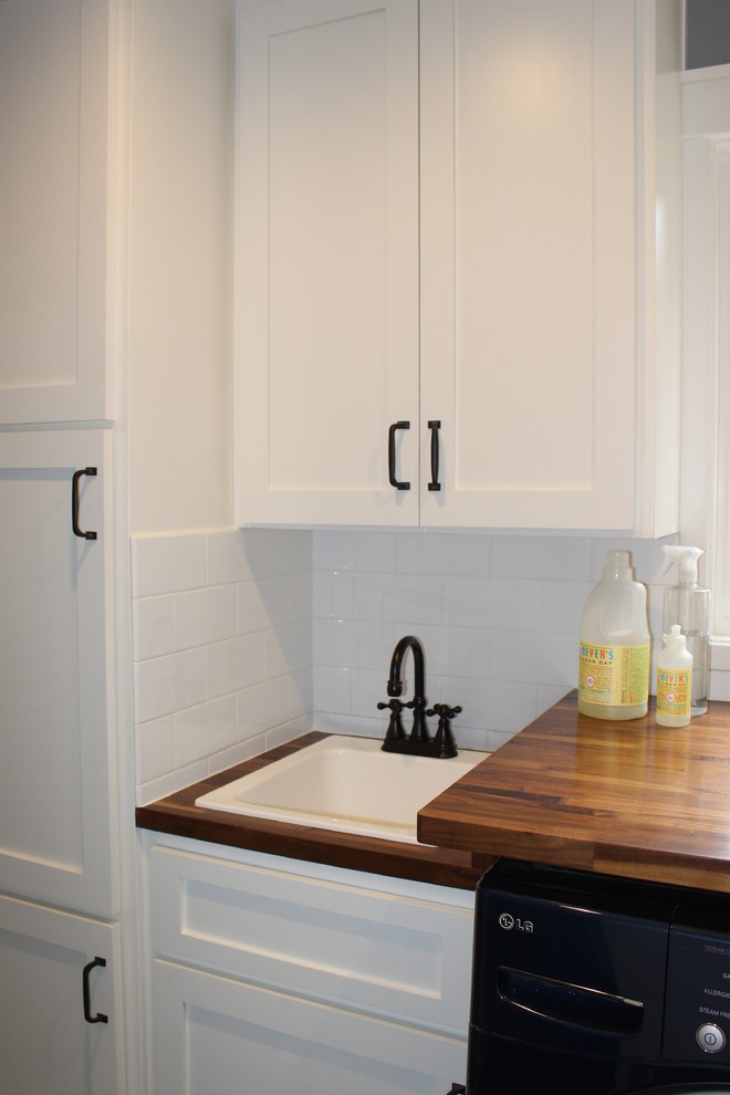This is an example of a small arts and crafts galley utility room in San Francisco with an undermount sink, shaker cabinets, white cabinets, wood benchtops, grey walls, porcelain floors and a side-by-side washer and dryer.