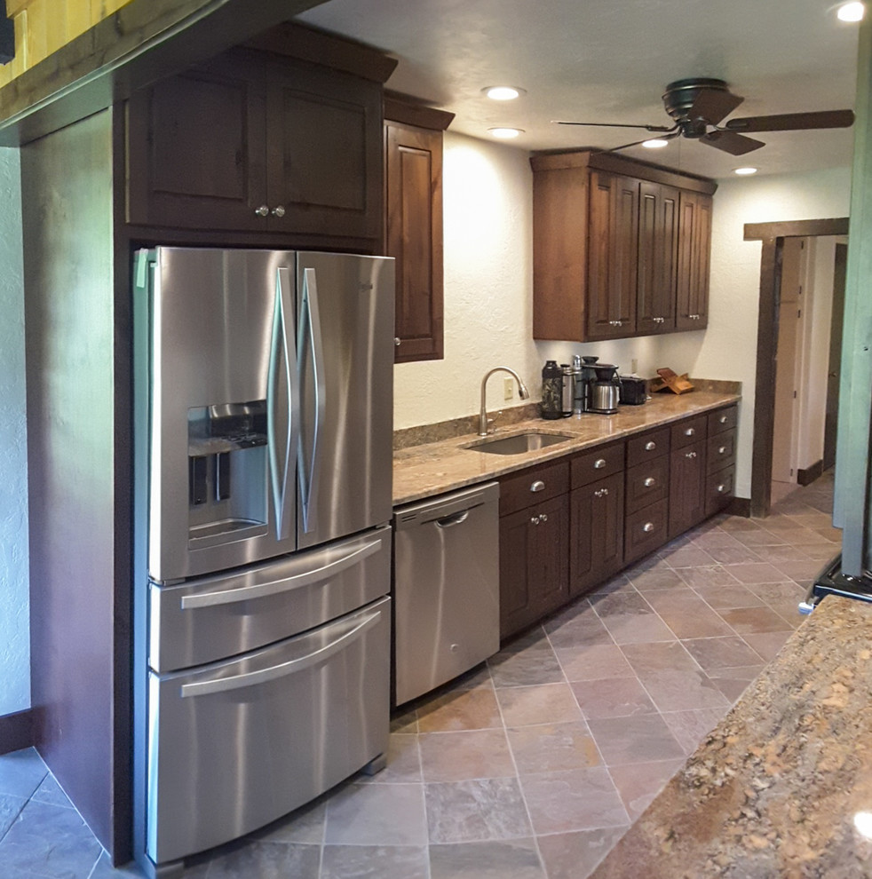 Example of a mid-sized mountain style galley slate floor and beige floor eat-in kitchen design with raised-panel cabinets, dark wood cabinets, granite countertops, an undermount sink, stainless steel appliances and no island