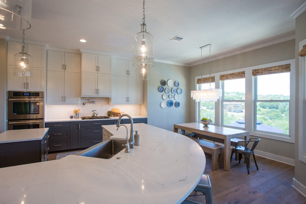 Eat-in kitchen - transitional light wood floor and beige floor eat-in kitchen idea in Austin with a farmhouse sink, shaker cabinets, white cabinets, quartz countertops, white backsplash, subway tile backsplash, stainless steel appliances and an island
