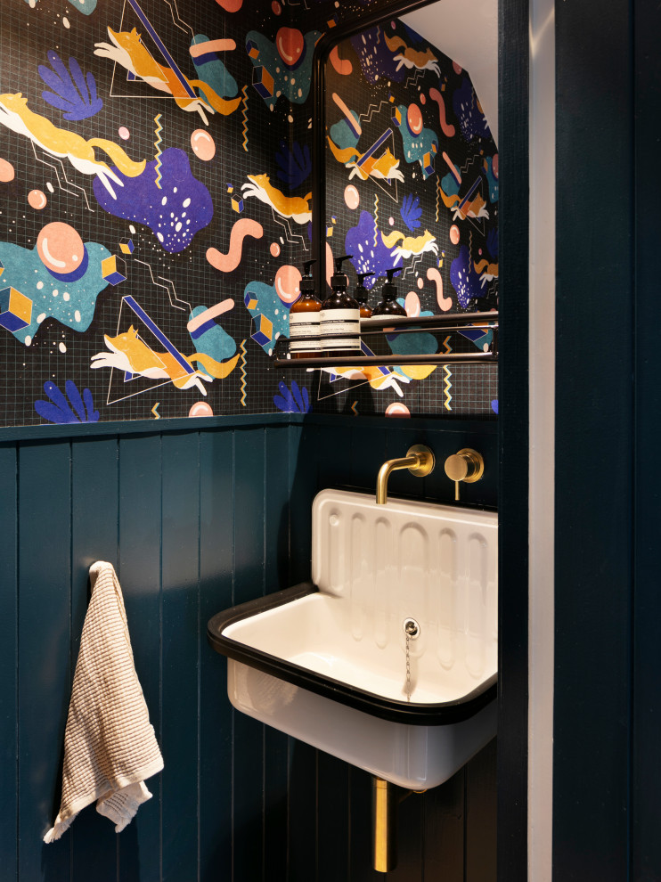 Small bohemian cloakroom in London with a wall mounted toilet, blue walls, dark hardwood flooring, a wall-mounted sink, brown floors, a feature wall and wallpapered walls.