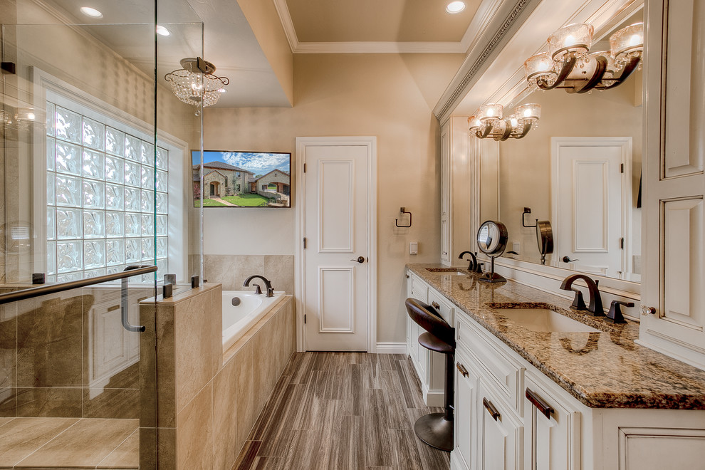 This is an example of a traditional master bathroom in Oklahoma City with an undermount sink, raised-panel cabinets, a drop-in tub, a corner shower and beige tile.