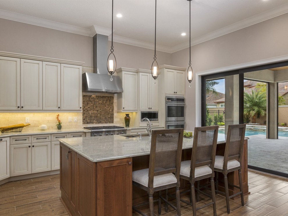 This is an example of a transitional open plan kitchen in Orlando with an undermount sink, raised-panel cabinets, white cabinets, granite benchtops, beige splashback, stone tile splashback, stainless steel appliances, porcelain floors and with island.