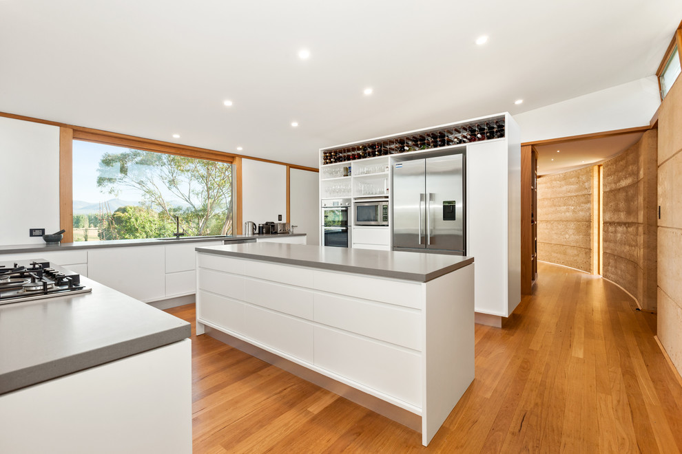 Design ideas for a large modern u-shaped kitchen in Central Coast with an undermount sink, white cabinets, quartz benchtops, grey splashback, stone slab splashback, stainless steel appliances, light hardwood floors, with island, brown floor and grey benchtop.