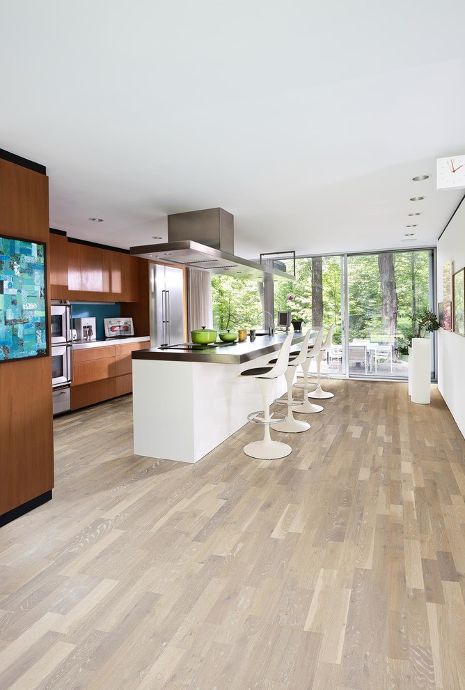 Large modern single-wall eat-in kitchen in New York with a farmhouse sink, flat-panel cabinets, brown cabinets, wood benchtops, blue splashback, subway tile splashback, stainless steel appliances, light hardwood floors, with island, grey floor and black benchtop.
