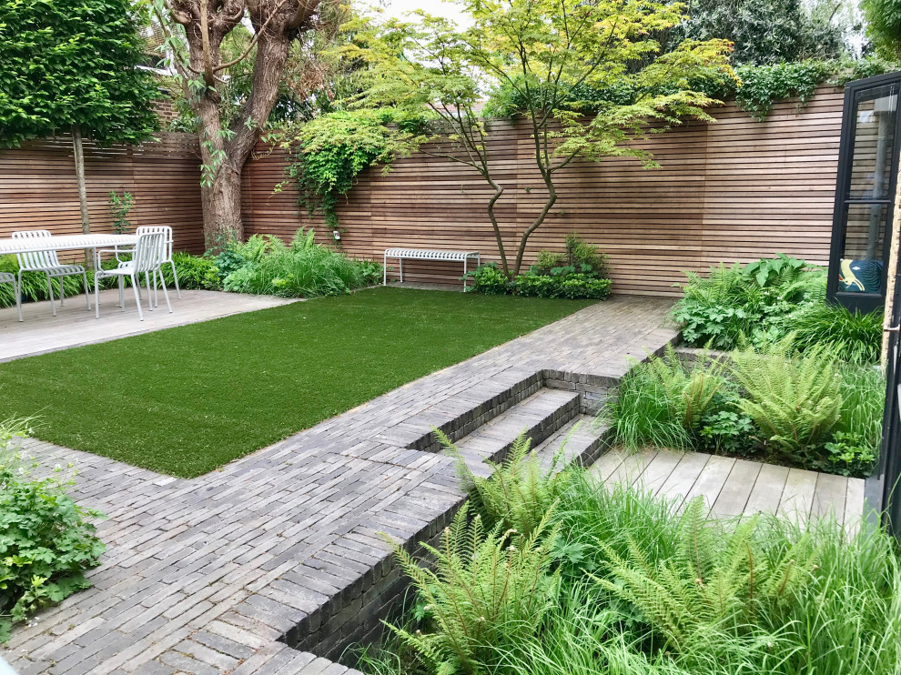 Geometrischer, Kleiner, Halbschattiger Moderner Garten im Sommer, hinter dem Haus mit Sichtschutz, Pflastersteinen und Holzzaun in London