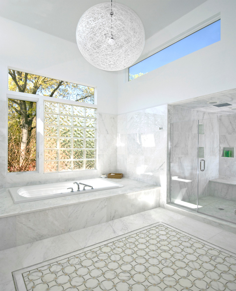 This is an example of a contemporary bathroom in New York with a drop-in tub, an alcove shower, white tile and marble.