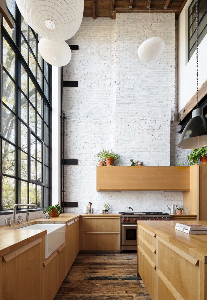 Design ideas for a large industrial l-shaped eat-in kitchen in New York with a farmhouse sink, flat-panel cabinets, wood benchtops, white splashback, brick splashback, stainless steel appliances, with island, brown floor, medium wood cabinets, dark hardwood floors and brown benchtop.