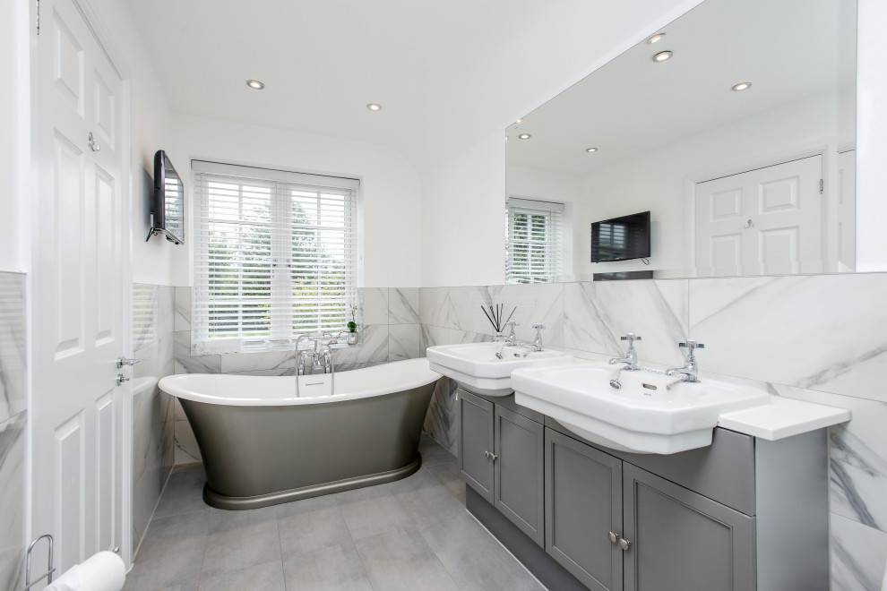 Design ideas for a mid-sized transitional master bathroom in Surrey with shaker cabinets, grey cabinets, a freestanding tub, gray tile, white walls, ceramic floors, a drop-in sink, quartzite benchtops, grey floor, white benchtops and a double vanity.