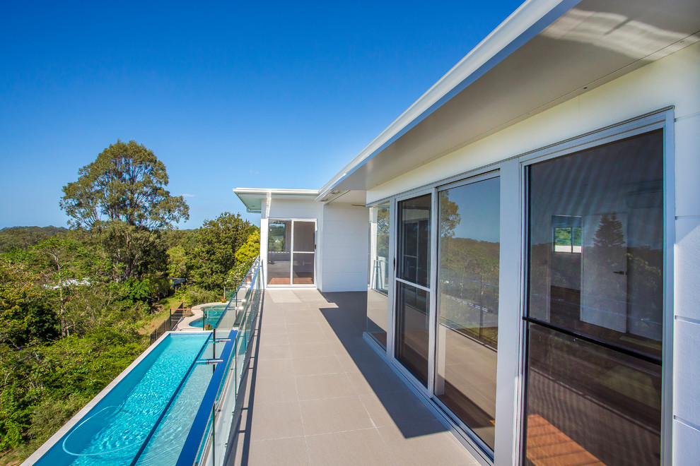Large contemporary balcony in Sunshine Coast with a roof extension and glass railing.