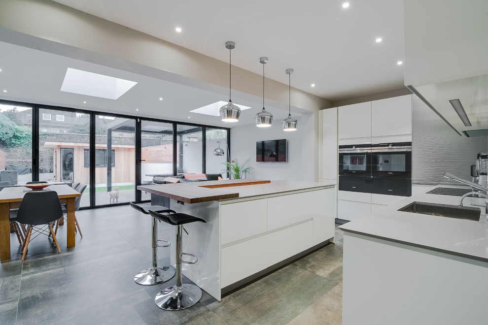 This is an example of a large modern l-shaped open plan kitchen in London with an undermount sink, flat-panel cabinets, white cabinets, solid surface benchtops, white splashback, stainless steel appliances, porcelain floors, with island and grey floor.