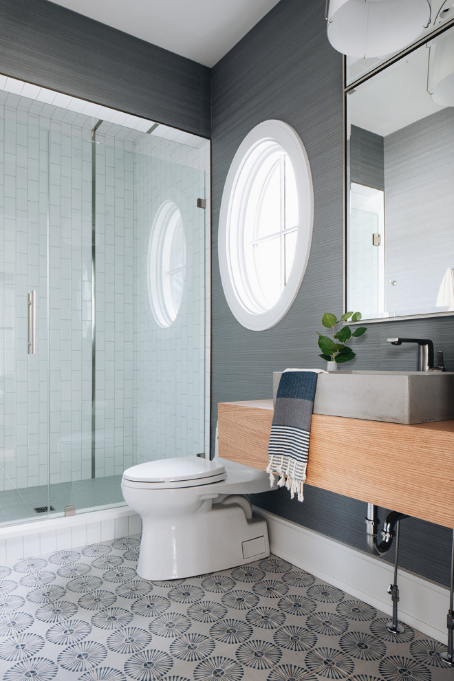 Photo of a mid-sized modern 3/4 bathroom in Chicago with brown cabinets, an alcove shower, a one-piece toilet, white tile, ceramic tile, blue walls, cement tiles, a vessel sink, wood benchtops, blue floor, a hinged shower door, a single vanity, a floating vanity and wallpaper.