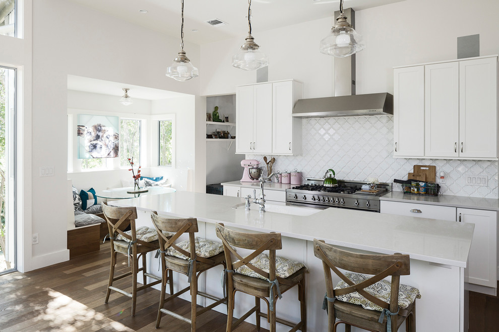 Mid-sized country l-shaped eat-in kitchen in Austin with shaker cabinets, white cabinets, white splashback, ceramic splashback, stainless steel appliances, medium hardwood floors, with island, a farmhouse sink, brown floor and quartz benchtops.