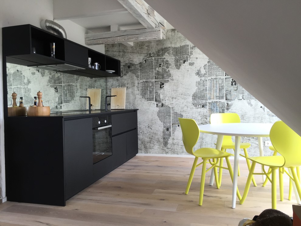 Mid-sized industrial single-wall eat-in kitchen in Cologne with flat-panel cabinets, black cabinets, mirror splashback, light hardwood floors, no island, black appliances, quartz benchtops, an integrated sink, multi-coloured splashback and brown floor.
