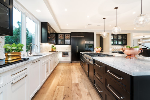 Dual-tone kitchen with white perimeter cabinets and dark (black) shaker island and base units, marble-look countertops, globe pendants, wide-plank wood flooring, and stainless range