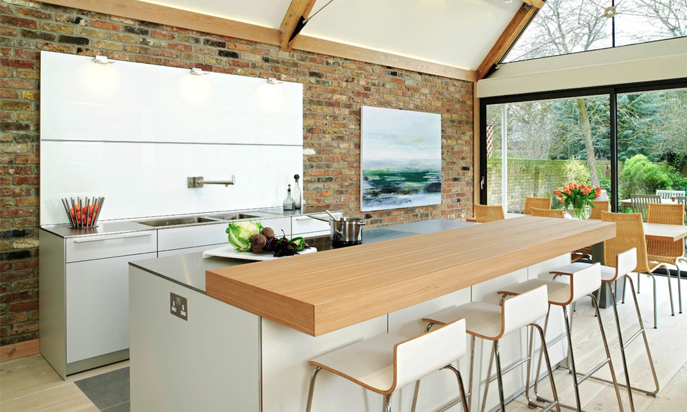 This is an example of a large contemporary eat-in kitchen in Other with flat-panel cabinets, white cabinets, white splashback, light hardwood floors, with island, a double-bowl sink and stainless steel benchtops.