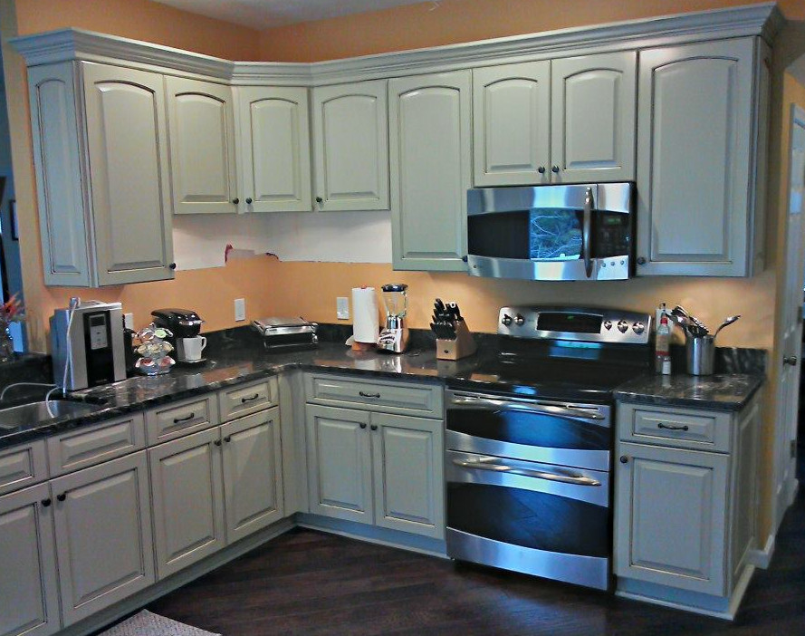 L-shaped dark wood floor eat-in kitchen photo with a drop-in sink, raised-panel cabinets, gray cabinets, granite countertops and stainless steel appliances