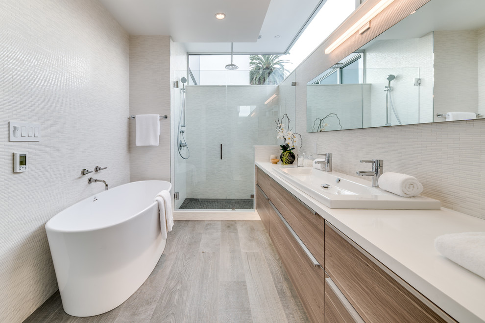 Mid-sized contemporary master bathroom in Los Angeles with flat-panel cabinets, light wood cabinets, a freestanding tub, white tile, glass tile, porcelain floors, a trough sink, engineered quartz benchtops, a hinged shower door, an alcove shower and grey floor.