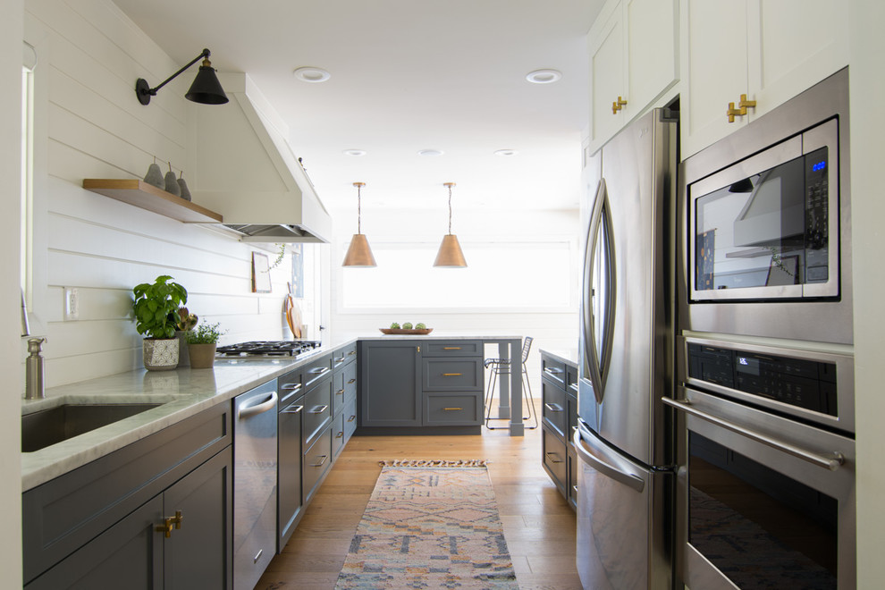 Inspiration for a mid-sized eclectic l-shaped eat-in kitchen in San Francisco with a drop-in sink, shaker cabinets, grey cabinets, marble benchtops, white splashback, stainless steel appliances, light hardwood floors, a peninsula and grey benchtop.