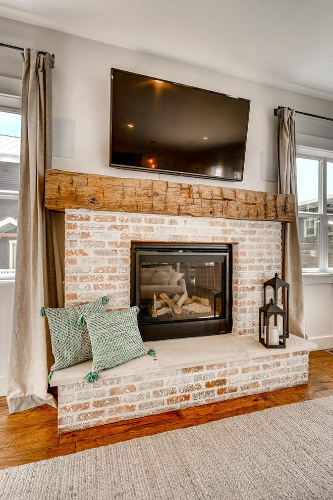 Photo of a mid-sized country open concept living room in Denver with grey walls, medium hardwood floors, a standard fireplace, a brick fireplace surround, a wall-mounted tv and brown floor.