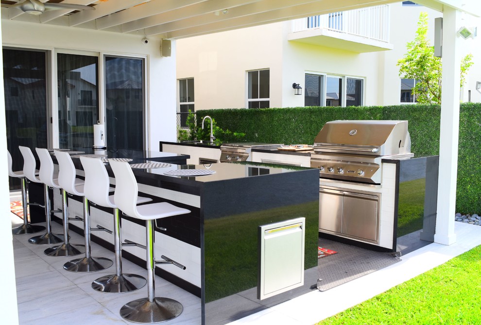 Photo of a mid-sized contemporary backyard patio in Miami with an outdoor kitchen, natural stone pavers and an awning.