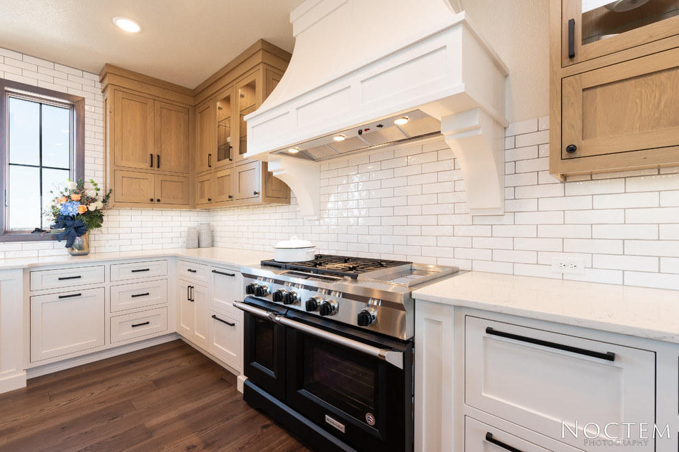 Transitional kitchen in Other with a farmhouse sink, recessed-panel cabinets, white cabinets, granite benchtops, white splashback, subway tile splashback, stainless steel appliances, with island, brown floor and white benchtop.