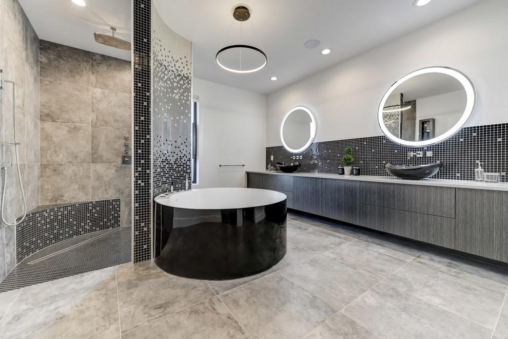 Photo of an expansive contemporary master bathroom in Edmonton with flat-panel cabinets, grey cabinets, a freestanding tub, a corner shower, black tile, black and white tile, gray tile, white walls, a vessel sink, grey floor, an open shower, mosaic tile, ceramic floors and solid surface benchtops.