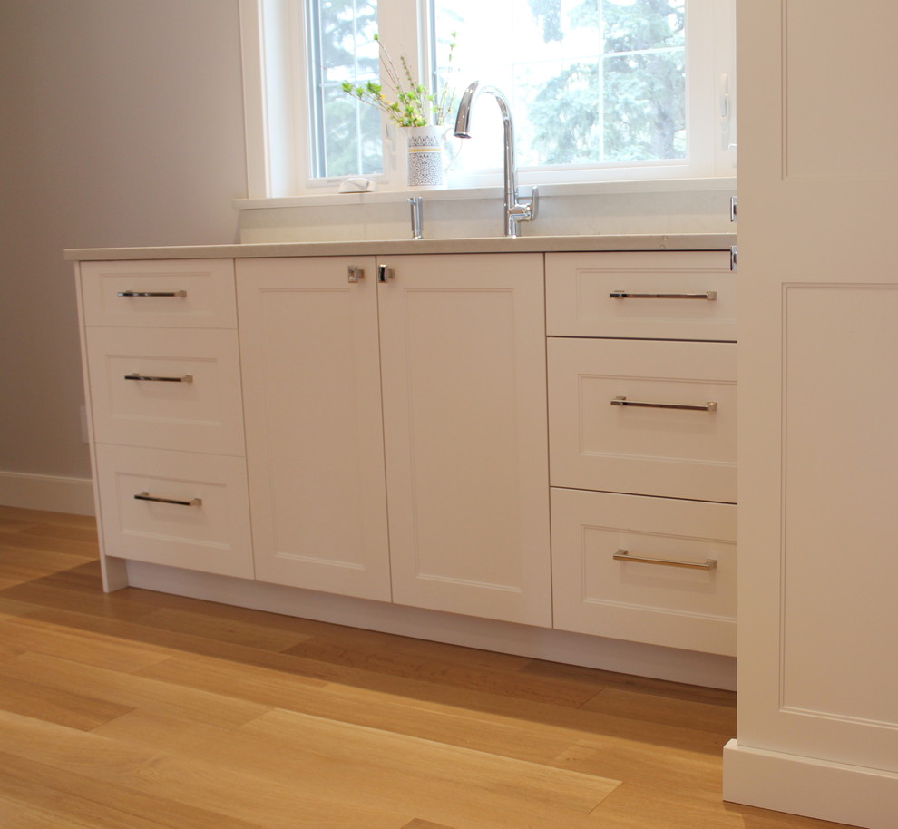 Example of a large transitional l-shaped light wood floor home design design with an undermount sink, shaker cabinets, white cabinets, quartz countertops, white backsplash, ceramic backsplash, stainless steel appliances and an island