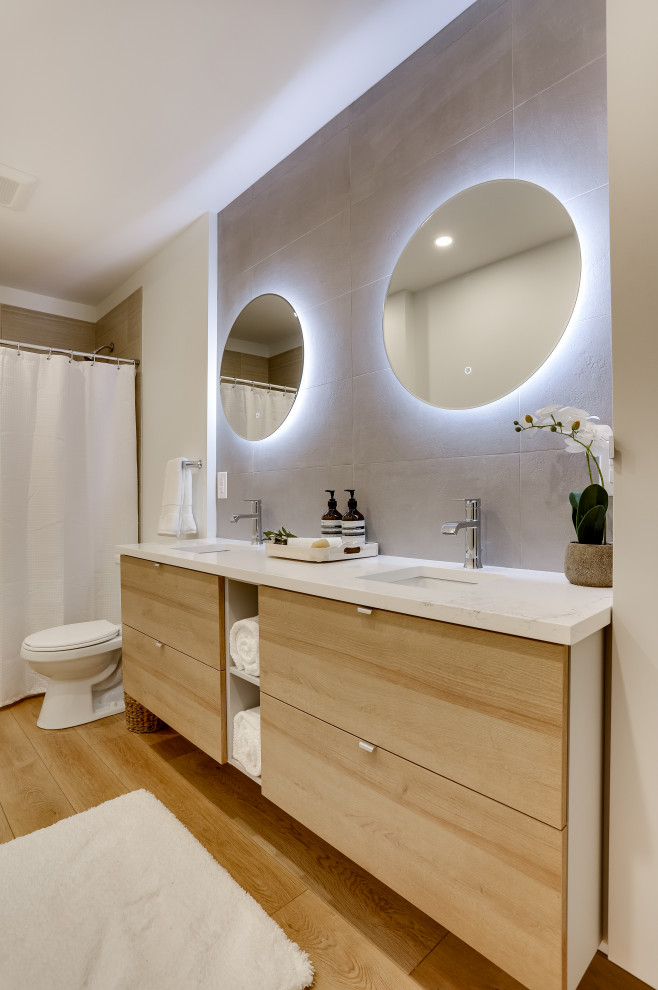 Photo of a mid-sized scandinavian bathroom in Vancouver with flat-panel cabinets, grey cabinets, an alcove tub, a shower/bathtub combo, gray tile, ceramic tile, white walls, vinyl floors, an undermount sink, quartzite benchtops, brown floor, white benchtops, a double vanity and a floating vanity.