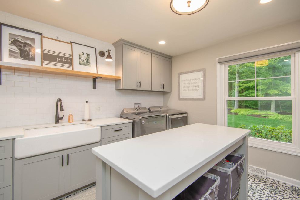 This is an example of an expansive utility room in Cleveland with a farmhouse sink, shaker cabinets, grey cabinets, white splashback, subway tile splashback, ceramic floors and a side-by-side washer and dryer.