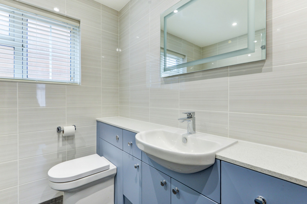 Inspiration för ett mellanstort funkis vit vitt badrum för barn, med släta luckor, blå skåp, ett badkar i en alkov, en dusch/badkar-kombination, en vägghängd toalettstol, beige kakel, keramikplattor, beige väggar, ett integrerad handfat, laminatbänkskiva och grått golv