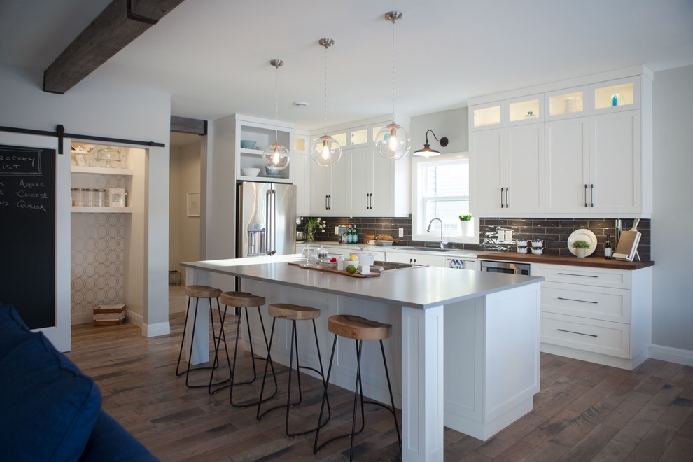 Inspiration for a large craftsman l-shaped dark wood floor and brown floor eat-in kitchen remodel with a drop-in sink, shaker cabinets, white cabinets, quartz countertops, gray backsplash, ceramic backsplash, stainless steel appliances and an island