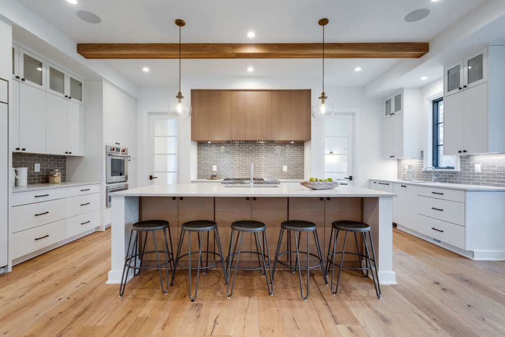 Photo of a country kitchen in DC Metro with flat-panel cabinets, white cabinets, grey splashback, subway tile splashback, stainless steel appliances, light hardwood floors, with island, beige floor and grey benchtop.