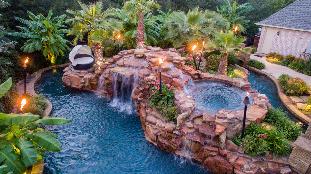 Design ideas for a large tropical backyard custom-shaped pool in Dallas with a water feature and natural stone pavers.