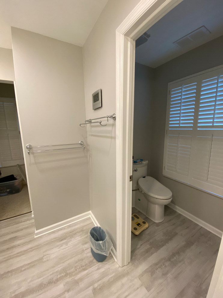 This is an example of a mid-sized transitional master bathroom in Cleveland with shaker cabinets, grey cabinets, a corner shower, a two-piece toilet, white tile, porcelain tile, grey walls, vinyl floors, an undermount sink, engineered quartz benchtops, grey floor, a hinged shower door, white benchtops, a shower seat, a double vanity and a built-in vanity.
