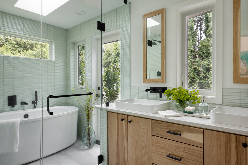 На фото: маленькая главная ванная комната в современном стиле с плоскими фасадами, светлыми деревянными фасадами, отдельно стоящей ванной, душевой комнатой, зеленой плиткой, стеклянной плиткой, белыми стенами, полом из цементной плитки, настольной раковиной, столешницей из кварцита, серым полом, душем с распашными дверями, белой столешницей, тумбой под две раковины и встроенной тумбой для на участке и в саду