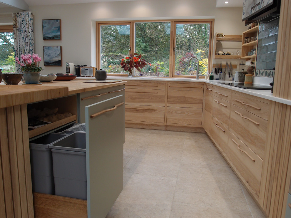 Photo of a large contemporary l-shaped open plan kitchen in Cornwall with a submerged sink, flat-panel cabinets, light wood cabinets, engineered stone countertops, blue splashback, black appliances, limestone flooring, an island, beige floors, white worktops, exposed beams and feature lighting.