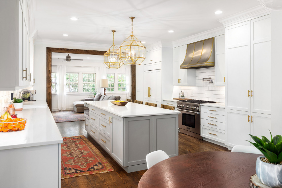Inspiration for a transitional galley dark wood floor and brown floor eat-in kitchen remodel with a farmhouse sink, shaker cabinets, white cabinets, white backsplash, stainless steel appliances, an island and white countertops